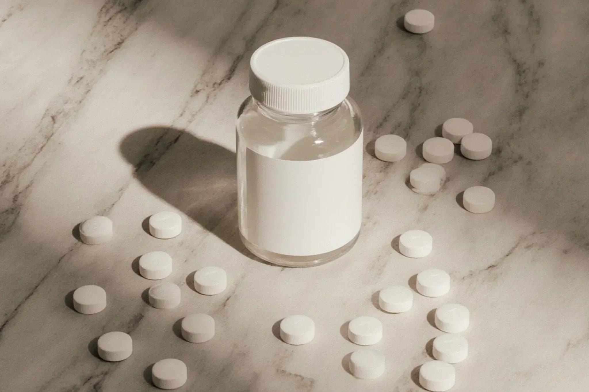 Clear supplement bottle with a white cap surrounded by scattered white tablets on a marble surface, illustrating dietary supplements such as biotin or vitamins often associated with skin and acne discussions.