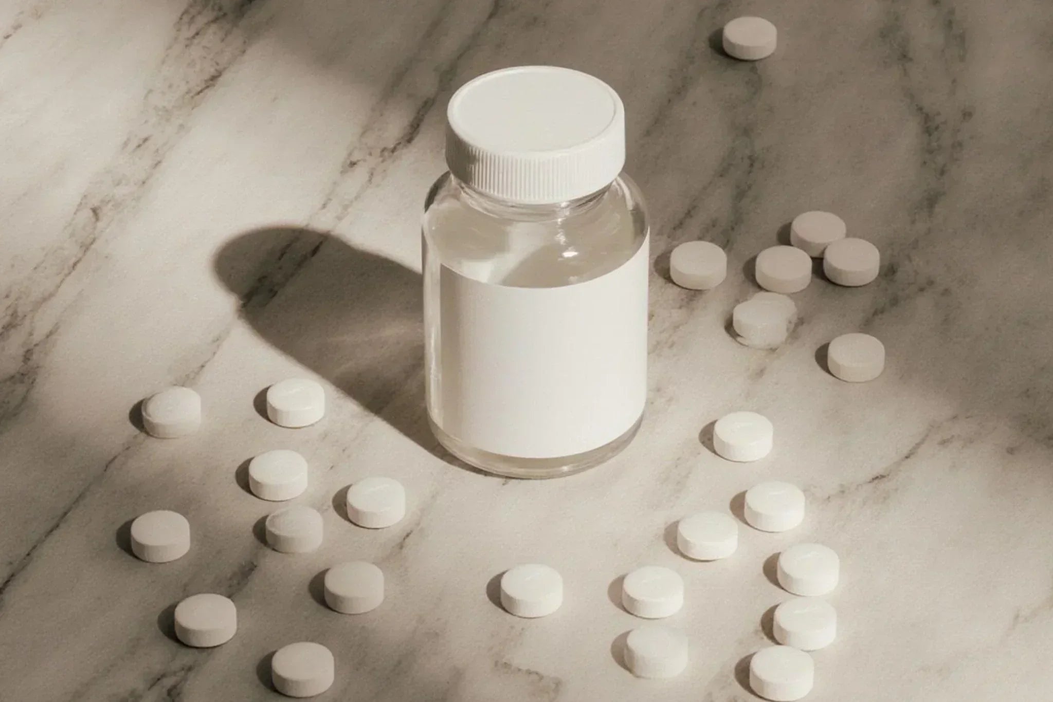 Clear supplement bottle with a white cap surrounded by scattered white tablets on a marble surface, illustrating dietary supplements such as biotin or vitamins often associated with skin and acne discussions.