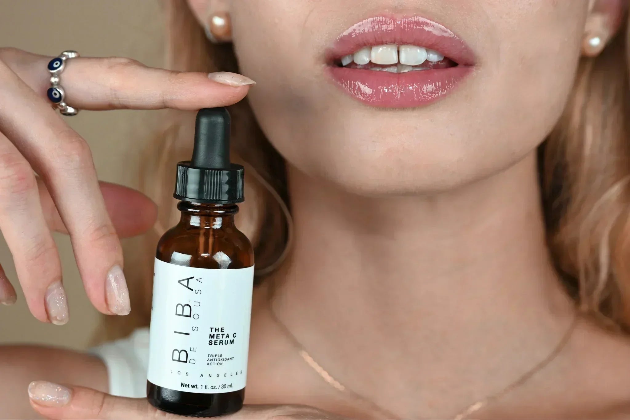 Model holding the BIBA de Sousa Meta C Serum bottle close to her face, showcasing application.