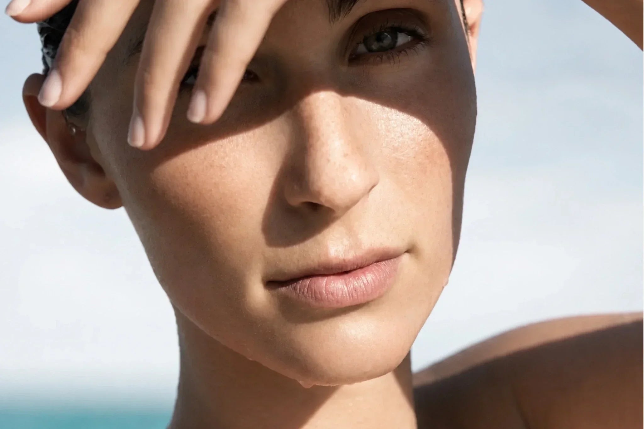 Woman shielding her face from the summer sun, illustrating the importance of sun protection and maintaining healthy skin during hot weather.
