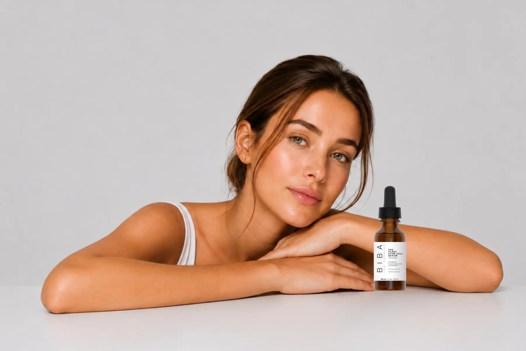 Woman with healthy-looking dry skin resting her head on folded arms against a light gray background with generous negative space, representing hydration, nourishment, and skincare for dry, dehydrated skin.
