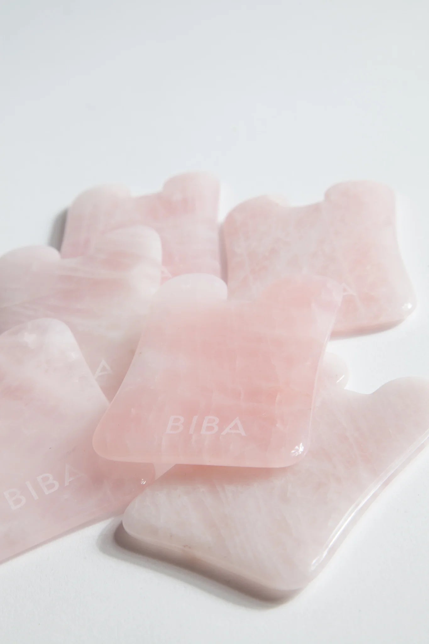 Group of Biba rose quartz gua sha facial boards arranged on a clean white surface, showcasing natural stone variations and polished finish.
