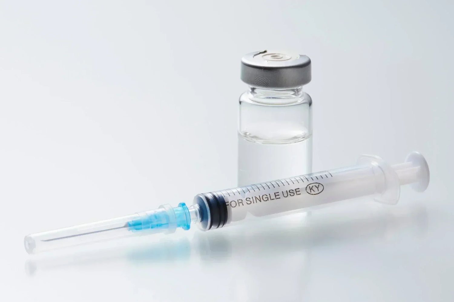 Glass vial and disposable syringe on a clean surface, representing injectable treatments in a clinical setting