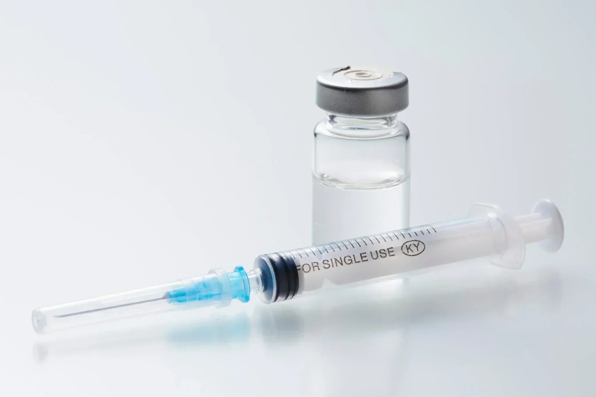 Glass vial and disposable syringe on a clean surface, representing injectable treatments in a clinical setting