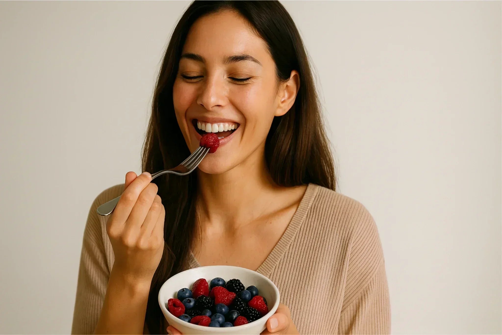 Smiling woman eating fresh berries from a bowl, demonstrating a healthy Mediterranean-style diet that supports glowing skin