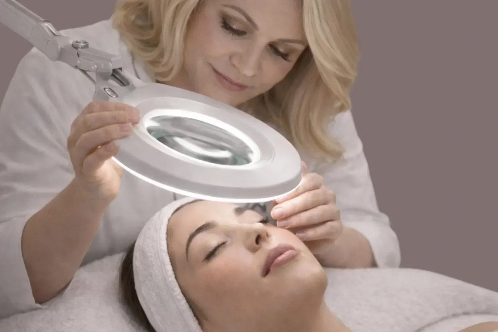 Professional esthetician performing a detailed skin analysis using a magnifying lamp during a facial treatment in a serene skincare studio.