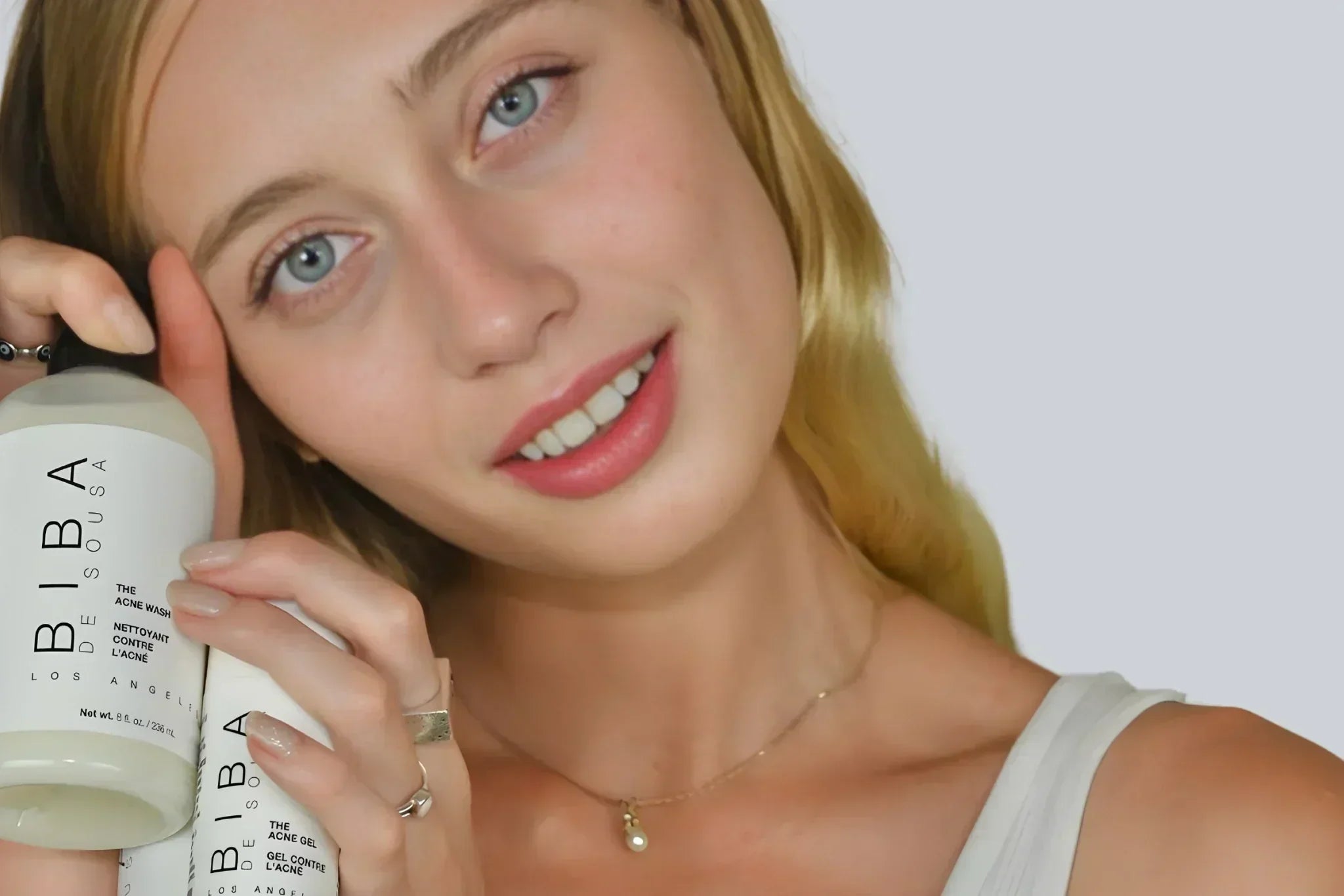 Woman holding Biba Los Angeles Acne Wash and Acne Gel, smiling at the camera.