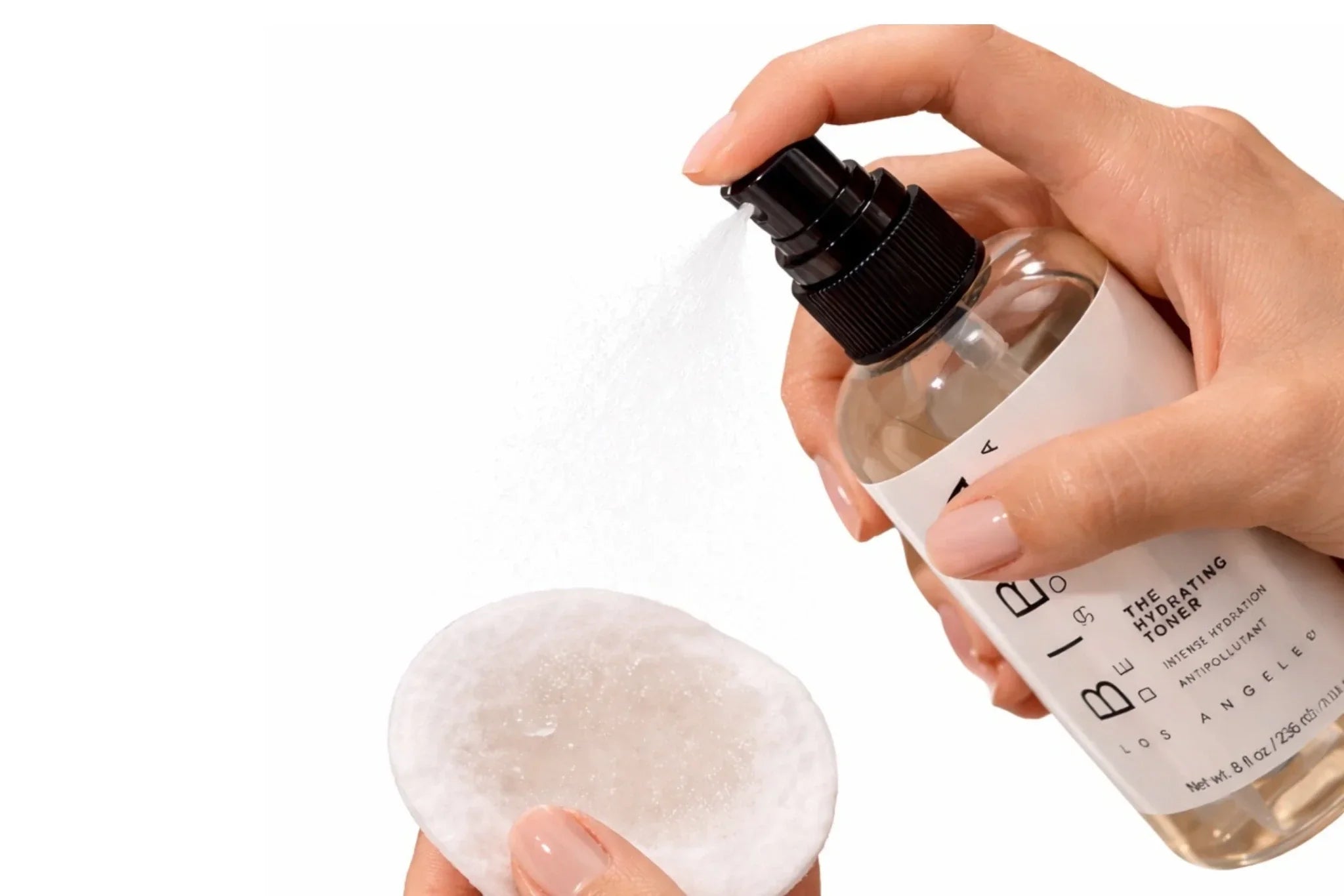 Hydrating toner being sprayed onto a cotton pad by hand, with fine mist visible against a clean white background, showcasing BIBA de SOUSA skincare bottle