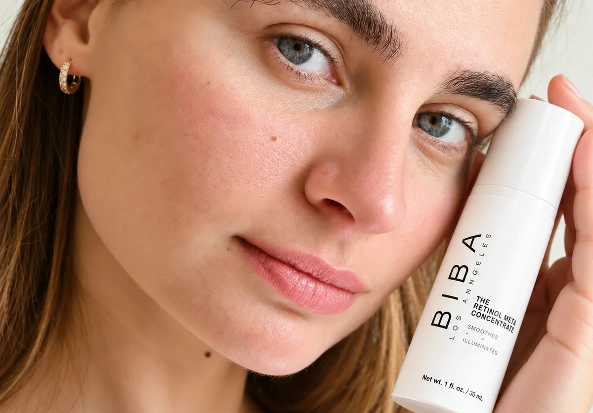 Woman holding Biba de Sousa Retinol Meta Concentrate in its new white packaging beside her face, highlighting a retinol skincare treatment for smoother texture and brighter-looking skin.