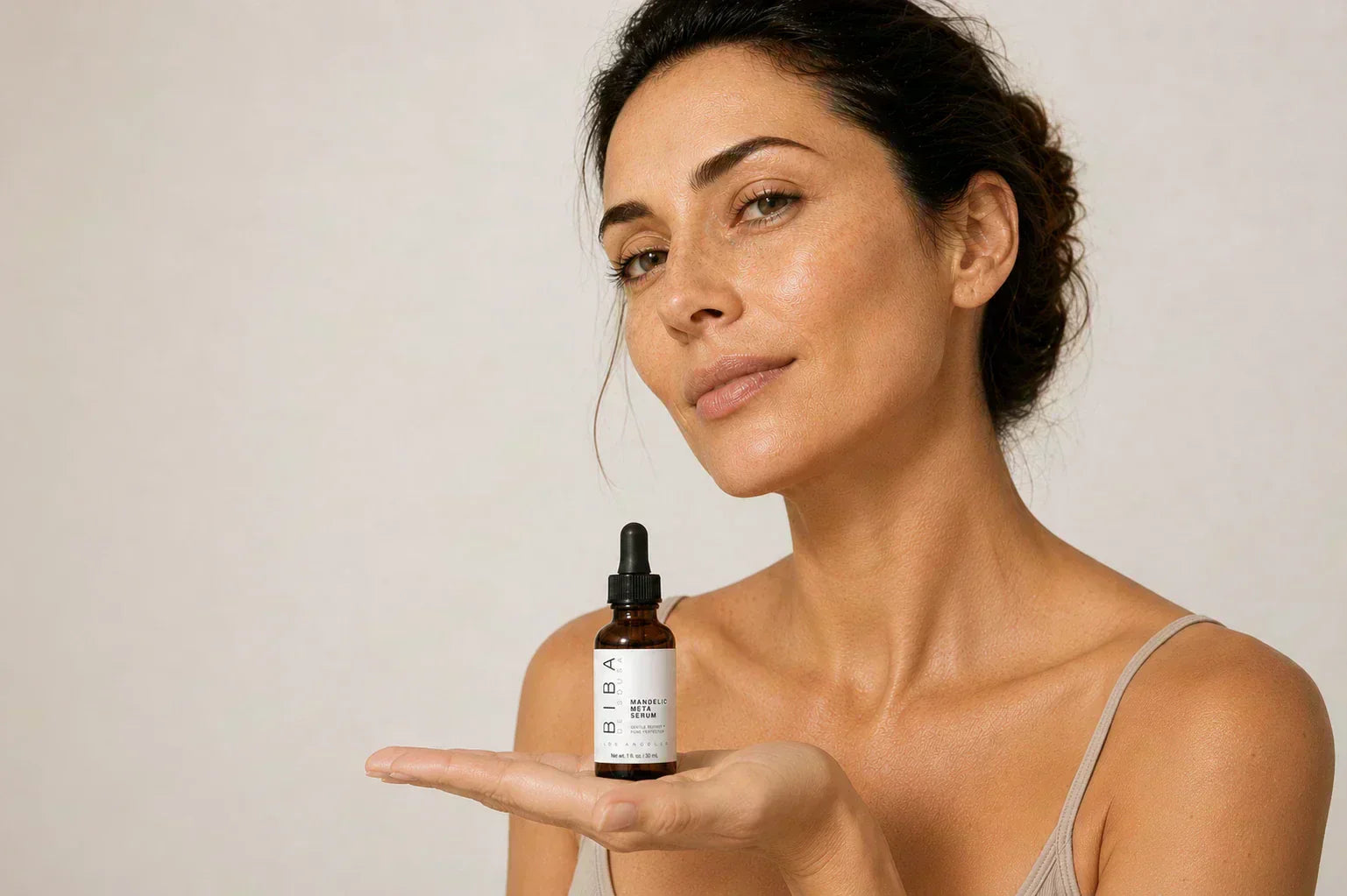 Woman with natural skin texture holding Biba Los Angeles Mandelic Meta Serum in the palm of her hand against a soft neutral background