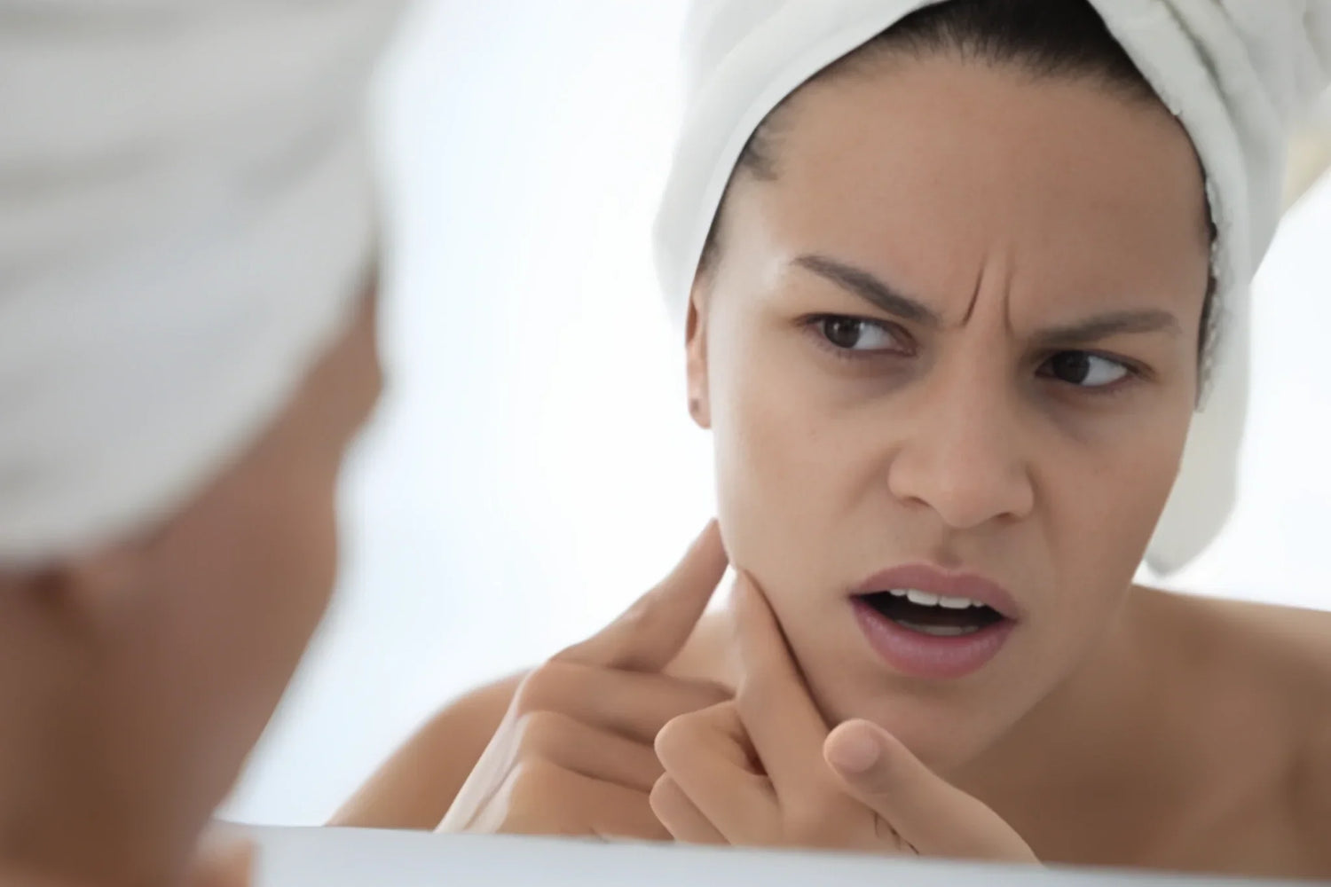 Woman looking closely at her skin in the mirror during a breakout, highlighting the connection between stress, inflammation, and skin health.