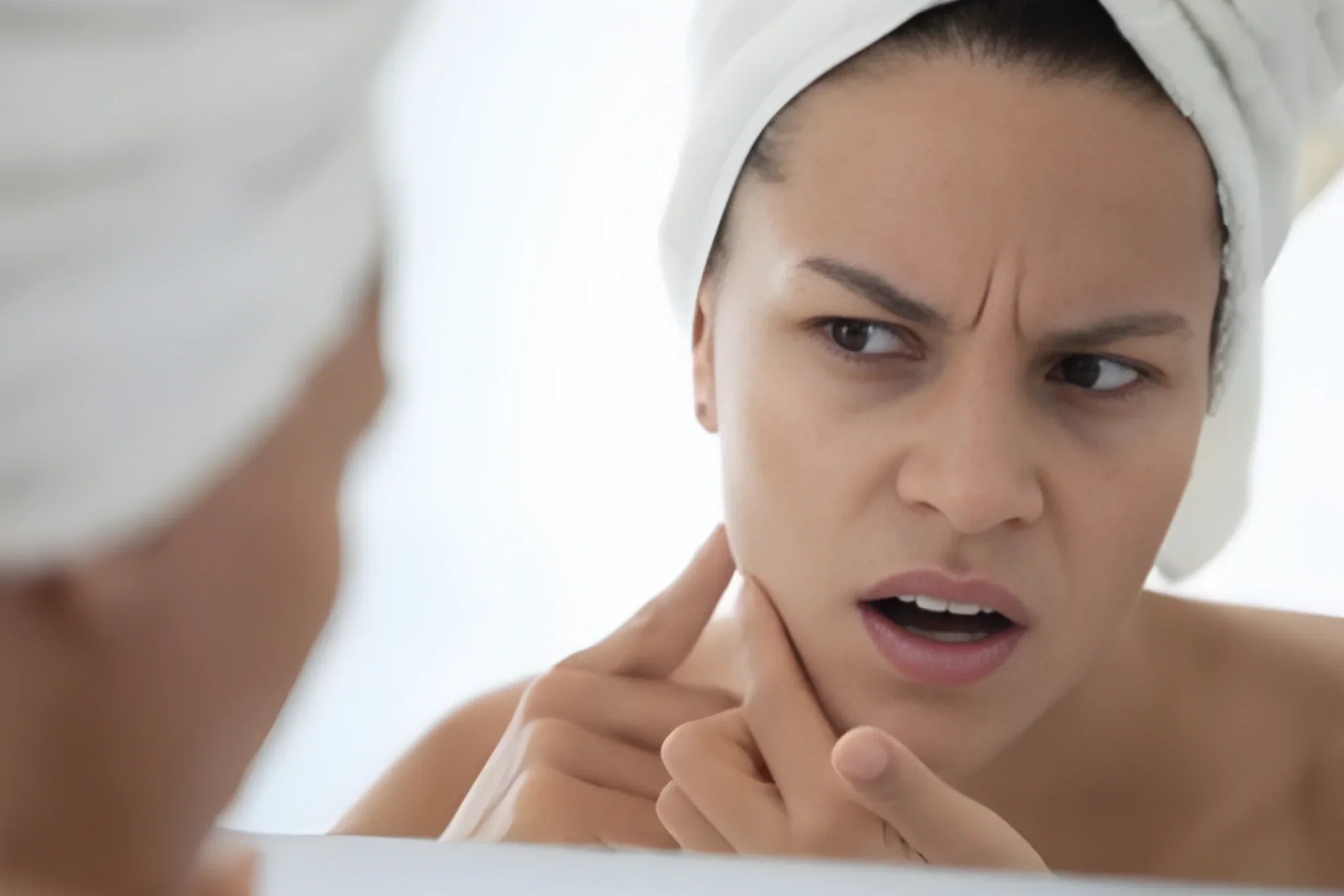 Woman looking closely at her skin in the mirror during a breakout, highlighting the connection between stress, inflammation, and skin health.