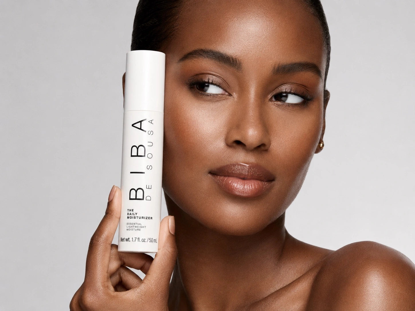 Model with healthy, radiant skin holding Biba Daily Moisturizer, a lightweight moisturizer designed for acne-prone, combination, and oily skin.