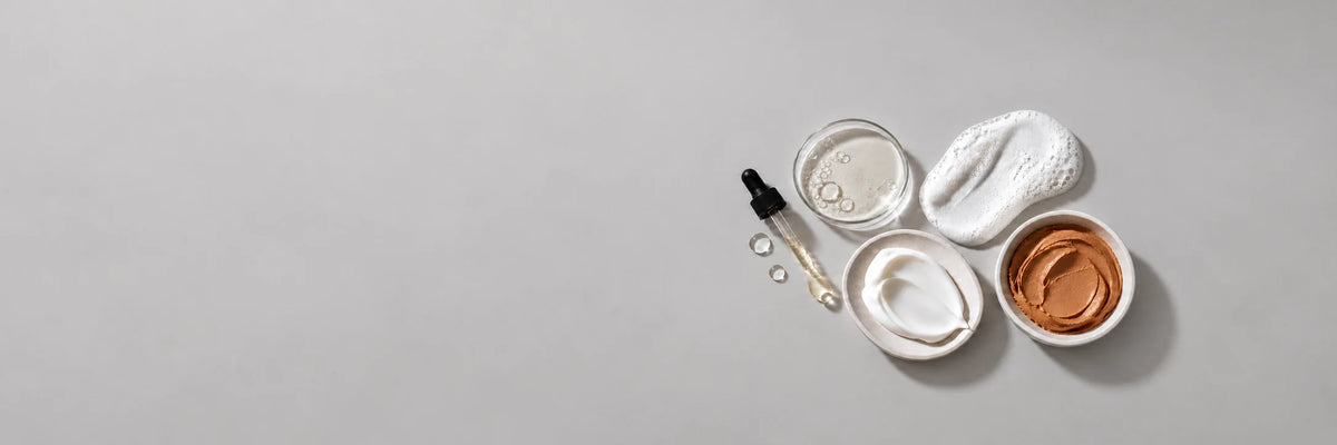 Flat lay of skincare textures featuring serum, foaming cleanser, moisturizer, and a pumpkin-colored mask