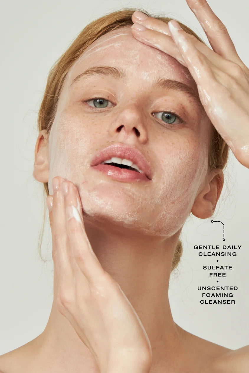 Woman gently massaging a foaming cleanser onto her face during cleansing routine, illustrating gentle daily cleansing with a sulfate-free, unscented foaming cleanser suitable for sensitive skin.